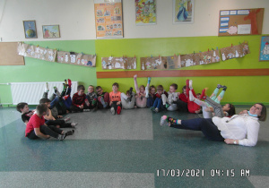 Zdjęcie grupowe klasy 1a. Uczniowie siedzą na podłodze i podnoszą w górę stopy w kolorowych skarpetkach.